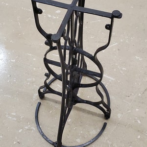 May include: Black metal table base with a circular design. The base has a cross-shaped top and a circular bottom.