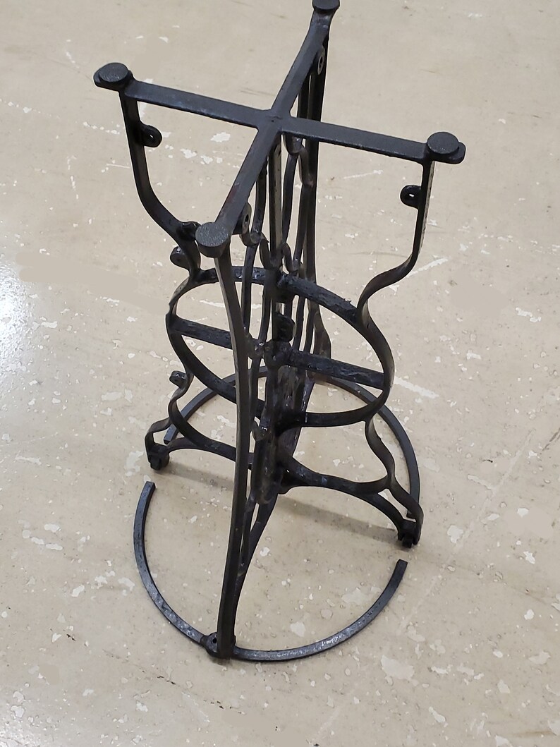 May include: Black metal table base with a circular design. The base has a cross-shaped top and a circular bottom.