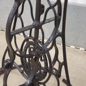 May include: Black cast iron sewing machine base with intricate details and a circular design on the bottom. The base is made of metal and has a black finish.