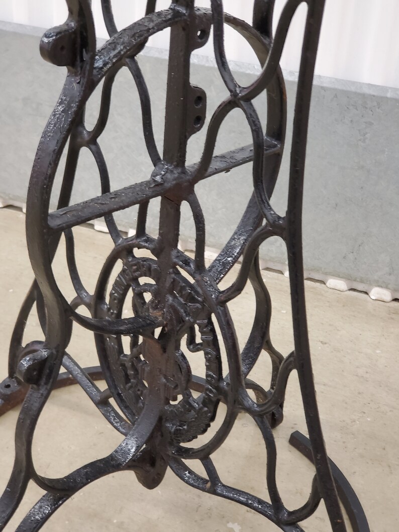 May include: Black cast iron sewing machine base with intricate details and a circular design on the bottom. The base is made of metal and has a black finish.