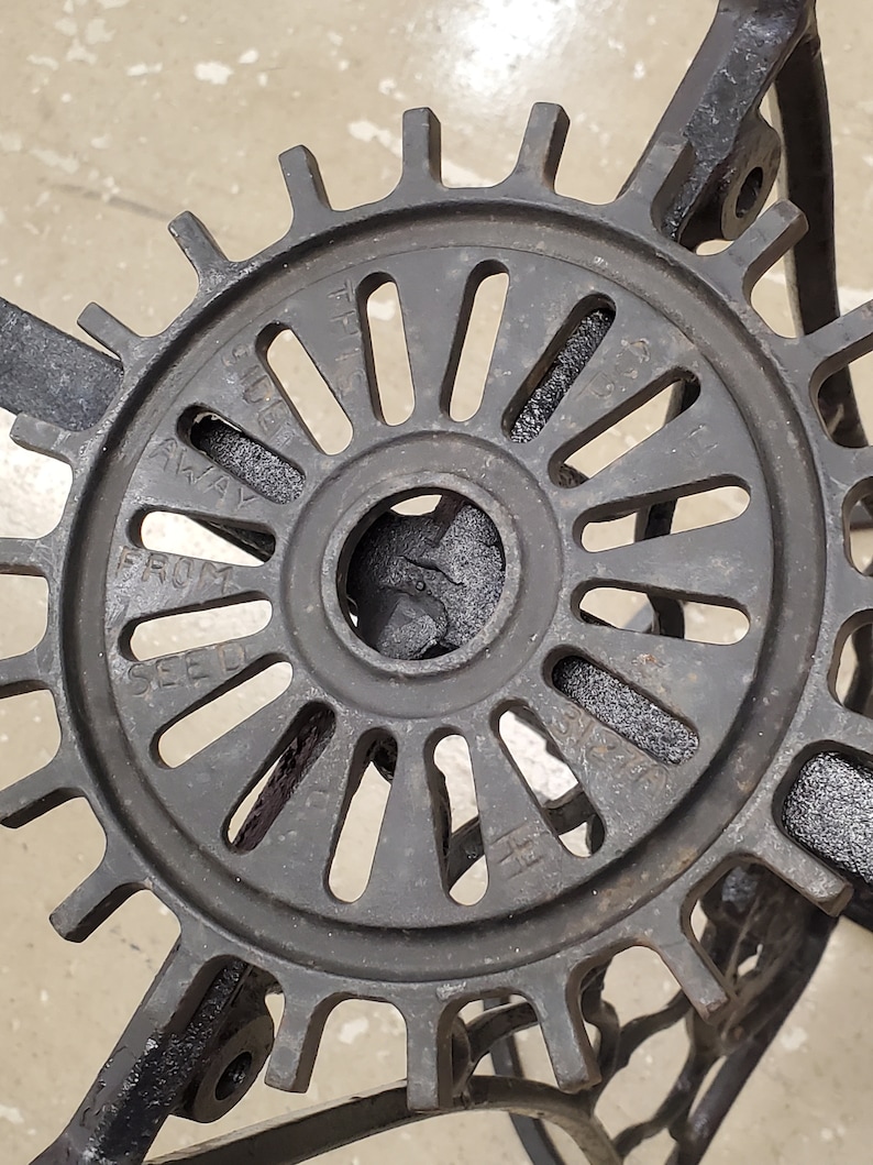 May include: Close-up of a black metal gear with the words "Seed" and "Away" visible on the surface. The gear has a circular shape with a central hole and a series of spokes radiating outwards.