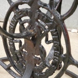 May include: Black metal stand with intricate details and a circular design featuring the text "Singer Manufacturing Co."