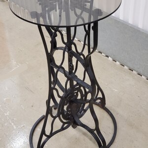 May include: A black metal table with a round glass top. The base of the table is made of intricate metalwork.