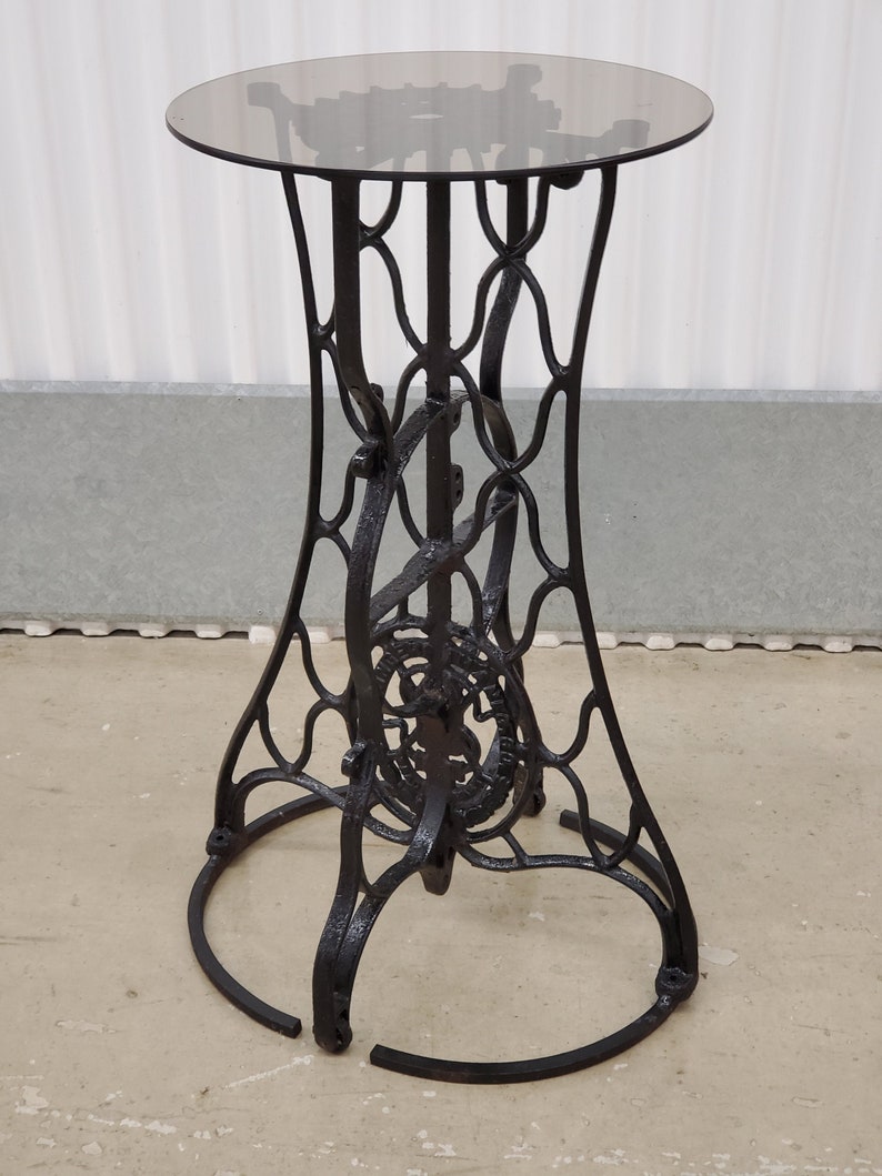 May include: Black metal side table with a round glass top. The table base is made from an old sewing machine stand.