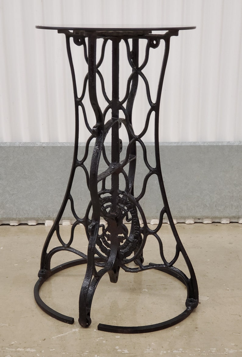 May include: Black metal table base with a circular top and intricate, decorative, openwork design. The base is made of cast iron and has a distressed finish.