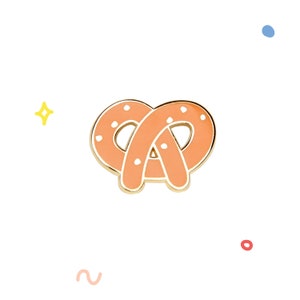 May include: A gold-colored enamel pin shaped like a pretzel. The pretzel is orange with white dots and a gold outline.