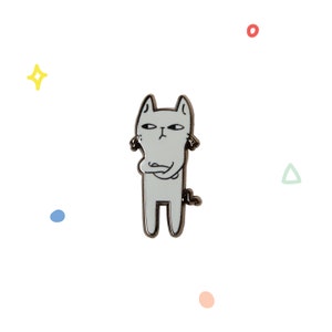 Può includere: Uno spillo in smalto bianco con un gatto dei cartoni animati con le braccia incrociate, che sembra infastidito. Il gatto ha un contorno nero e occhi neri.