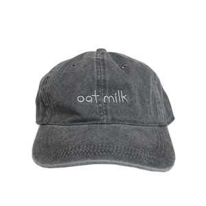 May include: A dark gray, distressed, cotton baseball cap with the text "oat milk" embroidered in white on the front.