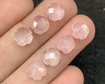 Puede incluir: Un conjunto de siete gemas rosas pálidas con forma de flor. Cada gema tiene una superficie facetada que captura la luz, creando un efecto brillante. Las gemas son ideales para la creación de joyas. Se destaca su delicado color y su intrincado diseño.