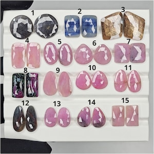 Op de afbeelding: Een verzameling gefacetteerde edelstenen in diverse vormen en kleuren. De collectie bevat ronde, rechthoekige en druppelvormige stenen in roze, blauwe en bruine tinten. Sommige stenen hebben een geometrische slijpvorm, andere een meer organische vorm.