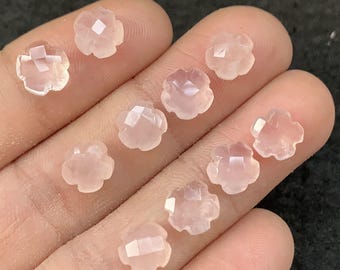 Puede incluir: Una colección de gemas en forma de flor de color rosa pálido. Cada gema tiene una superficie facetada, que captura la luz y crea un efecto brillante. Las gemas son pequeñas, delicadas y parecen ser cuarzo rosa.