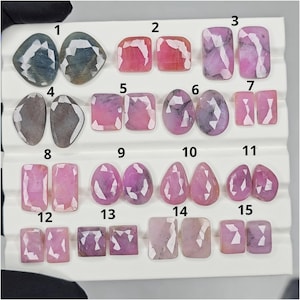 Puede incluir: Una colección de quince piedras preciosas en diversas formas y colores, incluyendo rosa, púrpura y gris. Las piedras preciosas están numeradas y dispuestas sobre una superficie blanca, mostrando sus facetas y claridad. Las formas incluyen ovaladas, rectangulares y de lágrima.