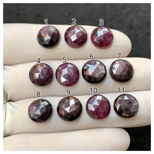 Puede incluir: Se muestran once piedras preciosas redondas y facetadas en varios tonos de rojo y púrpura. Cada piedra tiene un patrón único de facetas claras y oscuras. Las piedras preciosas están numeradas del 1 al 11.
