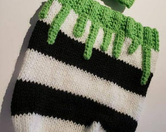 May include: A black and white striped knitted baby outfit with a green and white striped hat. The outfit has green dripping stripes on the top.