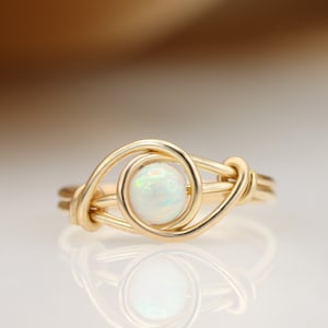 May include: A gold wire wrapped ring with a white opal gemstone in the center.