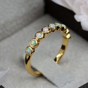 May include: A gold band ring with a row of small, round, white opals. The ring is in a white velvet ring box.
