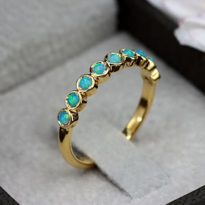 K&ouml;nnte beinhalten: Ein Goldring mit einer Reihe runder, hellblauer Opale. Der Ring befindet sich in einer schwarzen Samt-Ringbox.