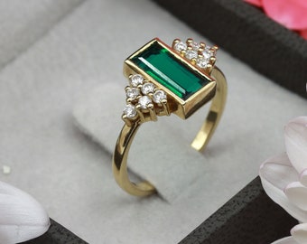 May include: A gold ring with a rectangular emerald green gemstone and small clear diamonds set in a geometric design.