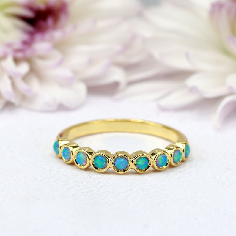K&ouml;nnte beinhalten: Ein Goldring mit einer Reihe von blaugr&uuml;nen Opal-Edelsteinen. Der Ring ist in einem schlichten, eleganten Stil gehalten.