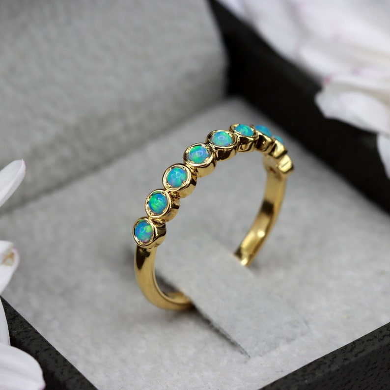 K&ouml;nnte beinhalten: Ein Goldring mit einer Reihe runder, hellblauer Opale. Der Ring befindet sich in einer schwarzen Samt-Ringbox.