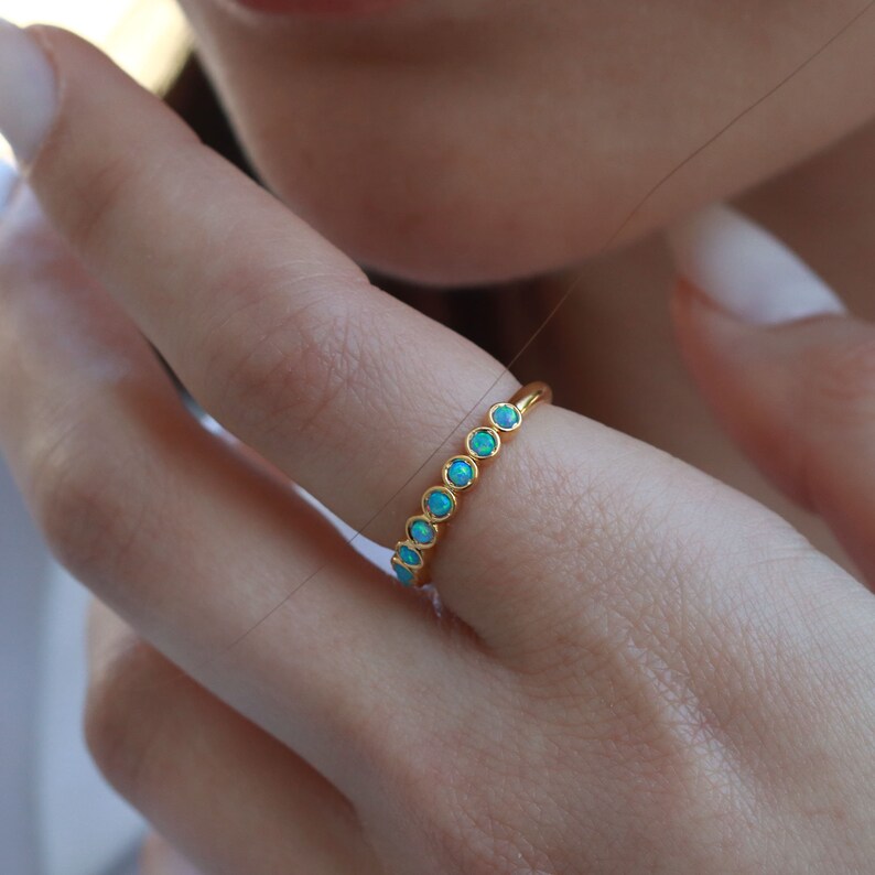 K&ouml;nnte beinhalten: Ein goldener Ring mit einer Reihe von hellblauen Opal-Steinen.