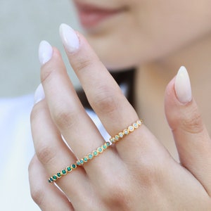 May include: Two gold rings with a row of small, round gemstones. One ring has green gemstones and the other has white gemstones.
