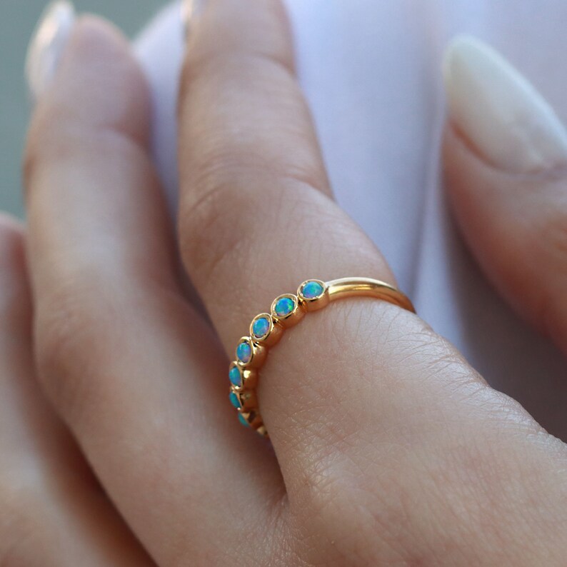 K&ouml;nnte beinhalten: Ein Goldring mit einer Reihe kleiner, runder, irisierender Opal-Steine.