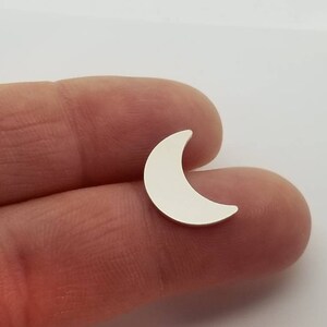 May include: A silver crescent moon charm, shown on a finger.