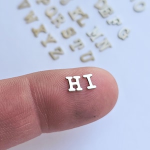 May include: Silver metal letters spelling "HI" on a finger.