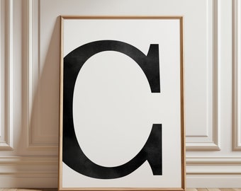May include: A framed black and white print of the letter C in a simple, bold font. The print is on a white background and is framed in a light wood frame.