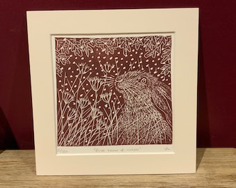 May include: A framed print of a linocut illustration of a rabbit in a field of tall grass with falling snow. The print is titled "First Snow of Winter" and is numbered 5/120.