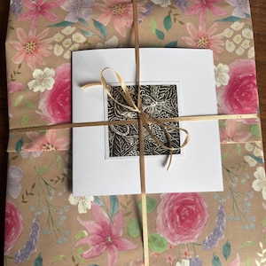 May include: A gift wrapped in brown paper with a floral pattern. The paper is tied with a gold ribbon and a white card with a black and white print of a butterfly is attached to the top.