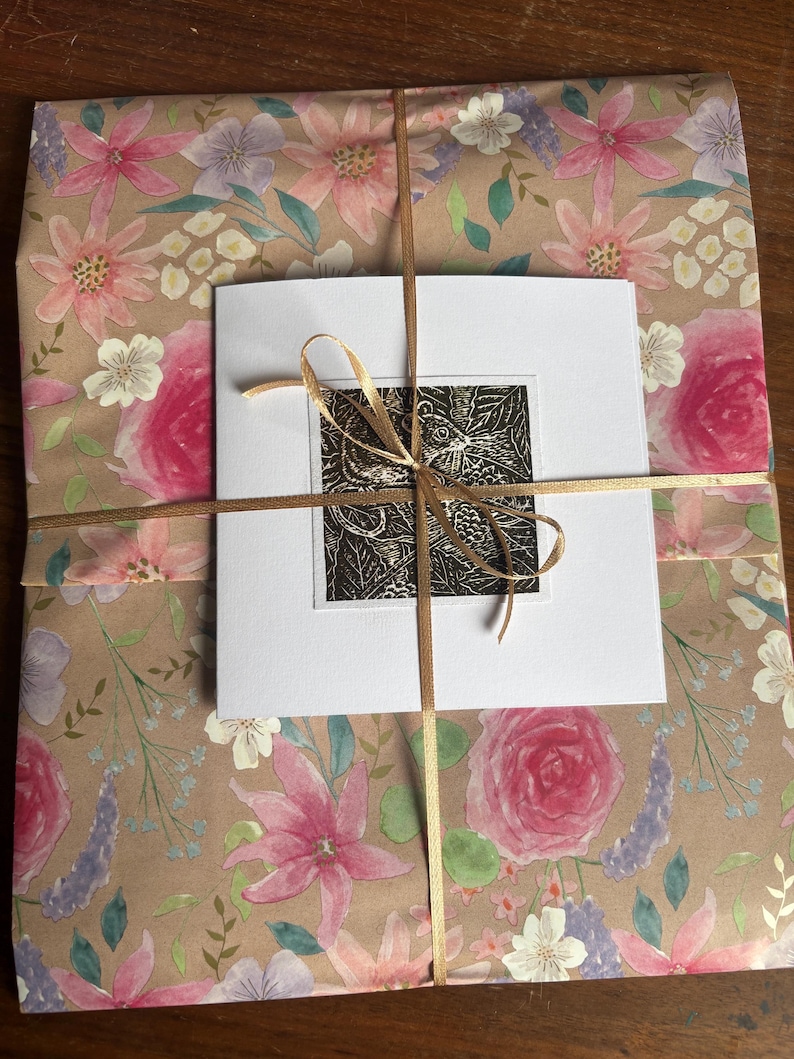 May include: A gift wrapped in brown paper with a floral pattern. The paper is tied with a gold ribbon and a white card with a black and white print of a butterfly is attached to the top.