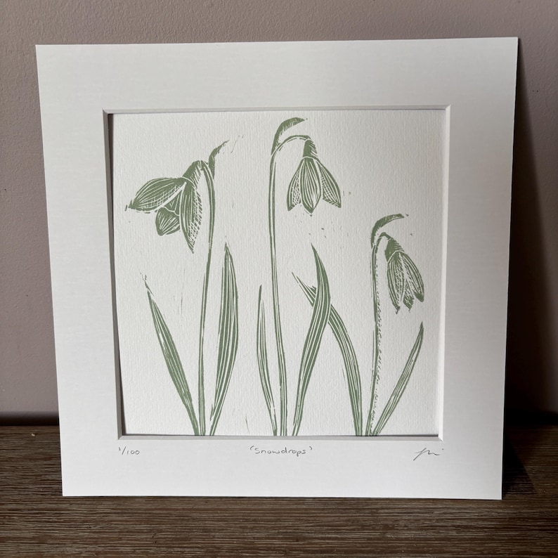 May include: A green and white print of snowdrops, a type of flower, with the text "Snowdrops" and "1/100" in the bottom corners.