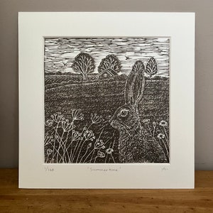 May include: A black and white linocut print of a rabbit in a field with a small house in the background. The print is titled "Summertime" and is numbered 1/120.