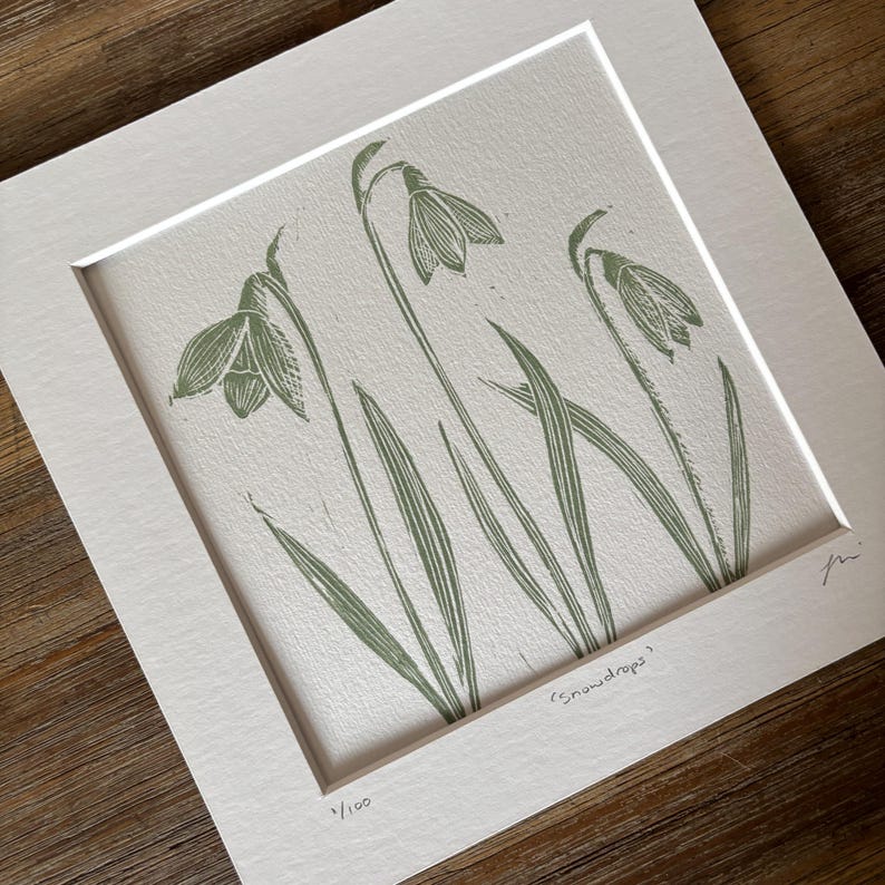 May include: A green and white print of snowdrops, a type of flower, with the text "snowdrops" and "1/100" in the bottom right corner.