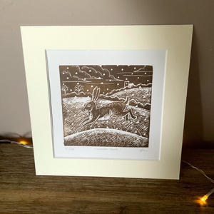May include: A framed brown and white print of a winter scene with a hare running through a snowy field. The print is titled "Winter Hare" and is numbered 51/100.