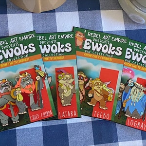 May include: Four colorful cards with the text "Rebel Art Empire Presents Ewoks Pin Collection From The TV Series!" and images of characters from the Star Wars Ewoks cartoon series. The characters are Chief Chirpa, Latara, Teebo, and Logray.