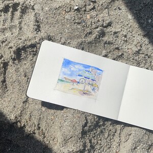 May include: A watercolor painting of a beach scene with an umbrella, a Ferris wheel, and buildings in the background.