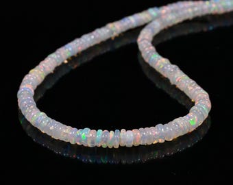 Könnte beinhalten: Eine Kette aus opalisierenden Opalperlen. Die Perlen sind klein, rund und haben eine milchig-weiße Grundfarbe mit schillernden Farbtönen. Die Halskette wird vor einem schwarzen Hintergrund präsentiert, der die Farben der Perlen hervorhebt.