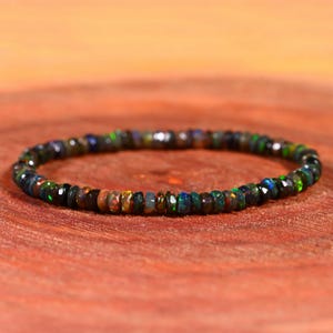 May include: A black opal gemstone bracelet with iridescent green, blue, and red hues. The bracelet is made of small, round beads and is strung on a clear elastic cord.