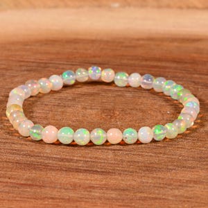 May include: A bracelet made of small, round opal beads. The beads are white, pink, and green, with iridescent flashes. The bracelet is strung on an elastic cord. The beads are approximately 0.6 cm in diameter, suitable for various wrist sizes.