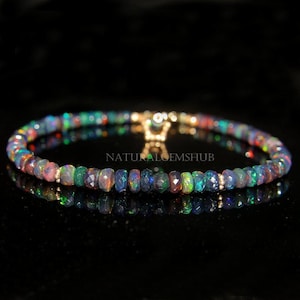 May include: A beaded bracelet featuring faceted opal gemstones in a variety of colors, including blue, green, and red. The bracelet has a gold clasp and is displayed on a reflective black surface. The text "NATURALGEMSHUB" is visible.