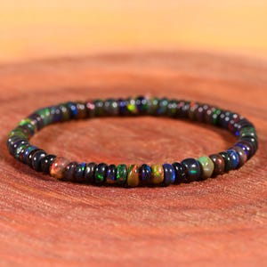 Puede incluir: Un brazalete de cuentas negras con piedras de ópalo iridiscente. El brazalete está hecho de pequeñas cuentas redondas que están enhebradas en un cordón delgado. Las cuentas son una mezcla de negro y ópalo iridiscente, lo que le da al brazalete un aspecto único y colorido.