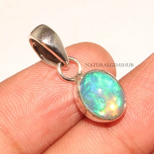May include: A silver pendant featuring a green opal gemstone with iridescent flashes of color. The pendant is oval shaped and set in a silver bezel. The pendant is attached to a silver bail.