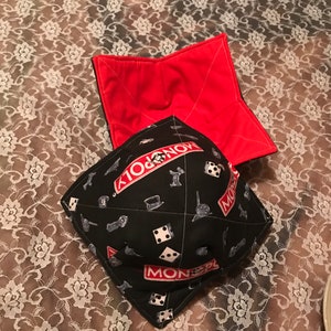 May include: A black and red fabric pot holder with a Monopoly game design. The pot holder is folded in half and has a red lining.