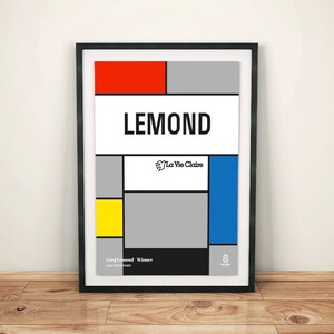 Może przedstawiać: Czarny plakat w ramie z geometrycznym wzorem w kolorze czerwonym, żółtym, niebieskim i szarym. Plakat zawiera tekst "LEMOND" i logo "La Vie Claire". Tekst "Greg Lemond Winner Tour de France 1986" znajduje się na dole plakatu.