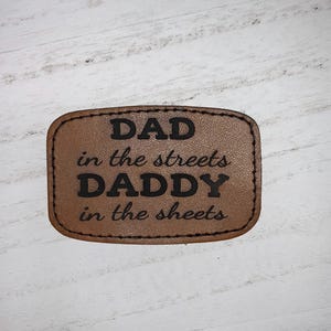 May include: Brown leather patch with the text "DAD in the streets DADDY in the sheets" in black lettering.