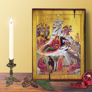 Puede incluir: Un icono cristiano ortodoxo tradicional que representa la Natividad de Jesús. El icono presenta una cueva con un pesebre, una estrella y varias figuras, incluyendo a María, José, pastores y ángeles. El icono está pintado en un estilo vibrante con acentos dorados.