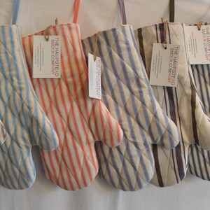 May include: Set of 10 striped oven mitts in various colors, including black, gray, blue, red, and white. The mitts are made of cotton and have a quilted design. Each mitt has a tag that reads "The Homestead Beck & Company".